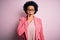 Young beautiful African American afro businesswoman with curly hair wearing pink jacket Looking fascinated with disbelief,