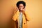 Young beautiful African American afro businesswoman with curly hair wearing yellow jacket covering ears with fingers with annoyed