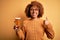 Young beautiful African American afro woman with curly hair drinking glass of beer happy with big smile doing ok sign, thumb up