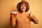 Young beautiful African American afro woman with curly hair drinking jar of beer happy with big smile doing ok sign, thumb up with