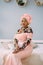 Young beautiful African lady wearing traditional pink dress and head turban, earrings and makeup, sitting on the bed in