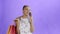 Young beautiful African using phone and holding shopping bags on purple Background in Studio. White dress with flowers