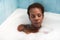 Young and beautiful Afro American woman takes a bubble bath in the bathtub. Beauty and hygiene concept