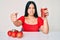 Young beautiful asian girl drinking glass of healthy tomato juice annoyed and frustrated shouting with anger, yelling crazy with