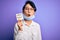 Young beautiful asian girl wearing medical mask holding reminder with virus alert message scared in shock with a surprise face,