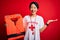 Young beautiful asian lifeguard girl using whistle holding orange life jacket over red background very happy and excited, winner