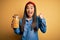 Young beautiful asian woman holding jar of Italian dry pasta macaroni over yellow background screaming proud and celebrating