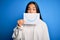 Young beautiful asian woman holding paper with smile draw on mouth over blue background scared in shock with a surprise face,