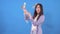 Young beautiful asian woman scatters paper banknotes dollars on a blue background slow mo