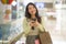 Young beautiful Asian woman shopping at modern mall - happy and attractive Korean girl holding shopping bags using mobile phone