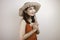 A young beautiful Asian woman wearing a straw hat gives greeting hands with a big smile on her face. Indonesian woman on white