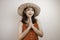 A young beautiful Asian woman wearing a straw hat gives greeting hands with a big smile on her face. Indonesian woman on white