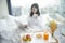 Young beautiful Asian woman is working and having small breakfast on the bed
