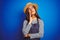 Young beautiful baker woman wearing apron and hat standing over isolated blue background with hand on chin thinking about