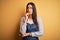 Young beautiful baker woman wearing apron uniform cooking over yellow background with hand on chin thinking about question,