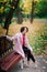 Young beautiful ballerina in fair coat and pointe shoes sit on the bench, rest outdoors