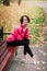 Young beautiful ballerina in fair coat and pointe shoes sit on the bench, rest outdoors