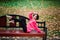 Young beautiful ballerina in fair coat and pointe shoes sit on the bench, rest outdoors