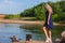 Young beautiful blond woman in blue mini dress and floral wreath standing and trying water on summer day with coutryside