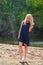 Young beautiful blond woman in blue mini dress and floral wreath standing and trying water on summer day with coutryside