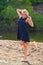 Young beautiful blond woman in blue mini dress and floral wreath standing and trying water on summer day with coutryside