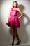 Young beautiful blond woman model with curly hair in pink dress and high heels shooes standing and looking at camera