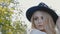 Young beautiful blond woman in white dress and dark hat posing. Attractive fashion model with loose hair. Slow motion.