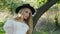 Young beautiful blond woman in white dress and dark hat posing. Attractive fashion model with loose hair. Slow motion.