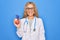 Young beautiful blonde cardiologist woman wearing stethoscope holding plastic heart looking positive and happy standing and