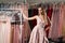 Young beautiful blonde girl wearing a full-length draped one shoulder pale pink satin slit prom ball gown decorated with