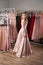 Young beautiful blonde girl wearing a full-length draped one shoulder pale pink satin slit prom ball gown decorated with