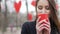 Young beautiful blonde hipster woman posing on the autumn park decorated with red paper hearts background drinking cup