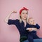 Young beautiful blonde mother with a cute baby. Conceptual gesture to show the biceps