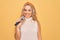 Young beautiful blonde singer woman singing using microphone over yellow background looking positive and happy standing and