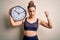 Young beautiful blonde sportswoman wearing sportswear on time to do sport holding clock annoyed and frustrated shouting with