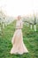 Young beautiful blonde woman in blooming garden. Pretty bride in elegant peach dress, posing on the background of