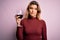 Young beautiful blonde woman drinking glasse of red wine over isolated pink background with a confident expression on smart face
