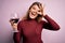 Young beautiful blonde woman drinking glasse of red wine over isolated pink background with happy face smiling doing ok sign with