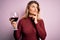 Young beautiful blonde woman drinking glasse of red wine over isolated pink background serious face thinking about question, very