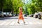 Young beautiful blonde woman in a red flower dress crosses the road at a crosswalk