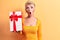 Young beautiful blonde woman wearing golden princess crown holding birthday gift scared and amazed with open mouth for surprise,
