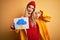 Young beautiful blonde woman wearing raincoat holding banner with cloud thunder image with angry face, negative sign showing