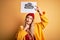 Young beautiful blonde woman wearing raincoat and wool cap holding banner with cloud image serious face thinking about question,