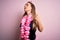 Young beautiful blonde woman wearing swimsuit and floral Hawaiian lei over pink background stretching back, tired and relaxed,