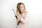 Young beautiful blonde woman wearing trendy pink dress using curling iron to make fashionable hairstyle on isolated