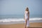 Young, beautiful, blonde woman in a white dress, walking on a lonely beach, relaxed and calm. Concept peace, tranquility, solitude