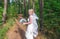 Young beautiful bride walk in green forest with bridal bouquet in white wedding dress