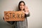 Young beautiful brunette activist woman protesting holding poster with strike message with open hand doing stop sign with serious