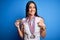 Young beautiful brunette atthete champion woman winning medals over blue background with surprise face pointing finger to himself