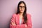 Young beautiful brunette businesswoman wearing jacket and glasses over pink background skeptic and nervous, disapproving